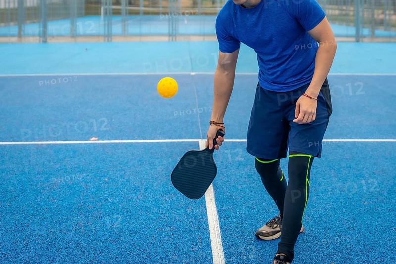 Man strikes a pickleball with his paddle on a vivid blue outdoor court, showcasing athletic movement, focus and active lifestyle during competitive recreational play