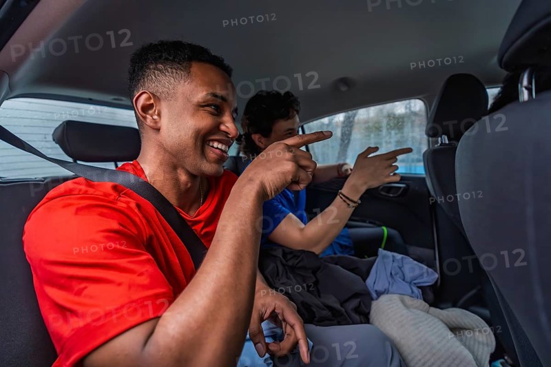 Young male pickleball players sharing a ride in a car, smiling and pointing while traveling together, expressing friendship, teamwork, and active lifestyle