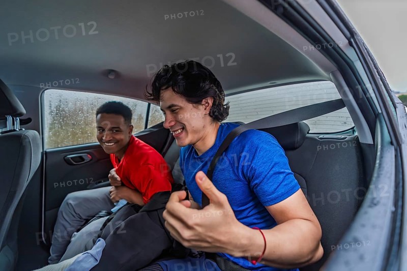 Two smiling diverse men friends wearing sportswear and fasten seatbelt in a car, traveling together and preparing for a pickleball game on a rainy day