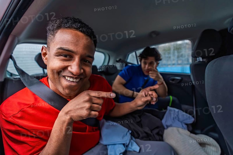 Young friends smiling and pointing from the backseat of a compact car, riding together and excitedly heading to play pickleball, enjoying a lively urban weekend trip