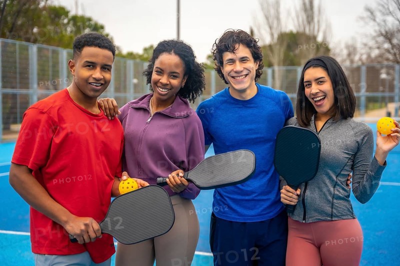 Group of diverse friends standing together on a bright blue pickleball court, smiling and holding paddles and balls, ready for an active and social leisure game outdoors