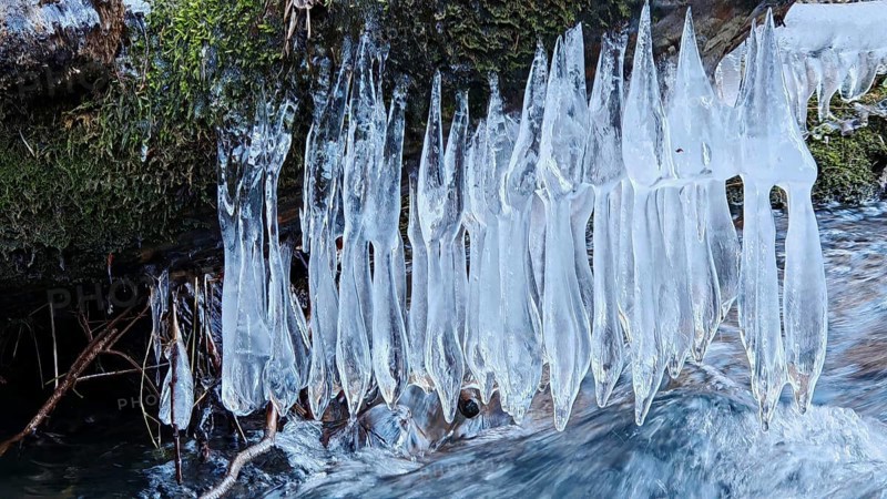 Icicles hang over a stream, framed by moss, winter view in nature, ice art, Franconian Forest nature park Park