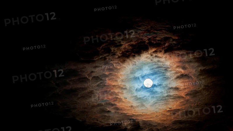 Full moon surrounded by dramatic, colorful clouds in the night sky