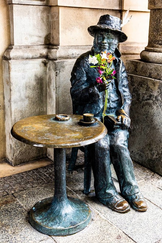 Life-size bronze sculpture as a memorial to Piotr Skrzynecki, Polish choreographer and cabaret director sitting at a coffee table, rynek with cloth halls, from 13th century, main market, city landmark, Krakow, Poland