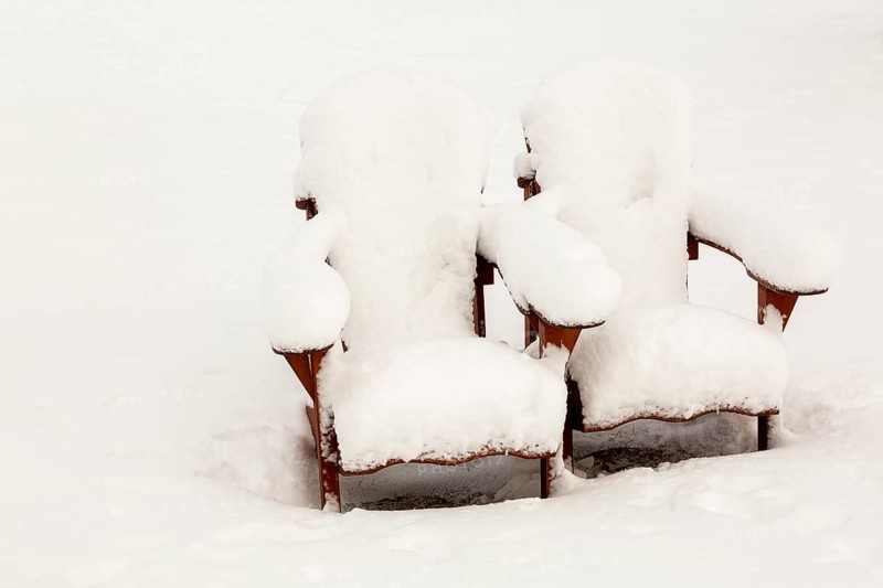 Two brown stained wooden Adirondack chairs covered in freshly fallen winter like snow in public park in late autumn, Quebec, Canada