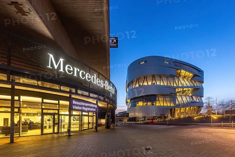 The Mercedes-Benz Museum in Stuttgart presents a journey through the automotive history of the global corporation. Spectacular architecture of the Automobile Museum in the evening. On the left, the entrance to the Mercedes-Benz Group AG factory premises. Stuttgart, Baden-Württemberg, Germany