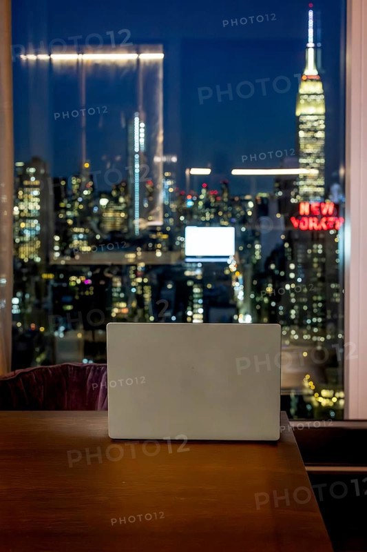 Laptop resting on a wooden desk, overlooking the illuminated cityscape of manhattan and the iconic empire state building at night, representing remote work, business, and urban living