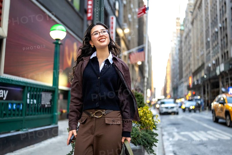 Young professional businesswoman smiling, walking confidently along a bustling street in manhattan, embracing the urban environment near a subway entrance in new york city