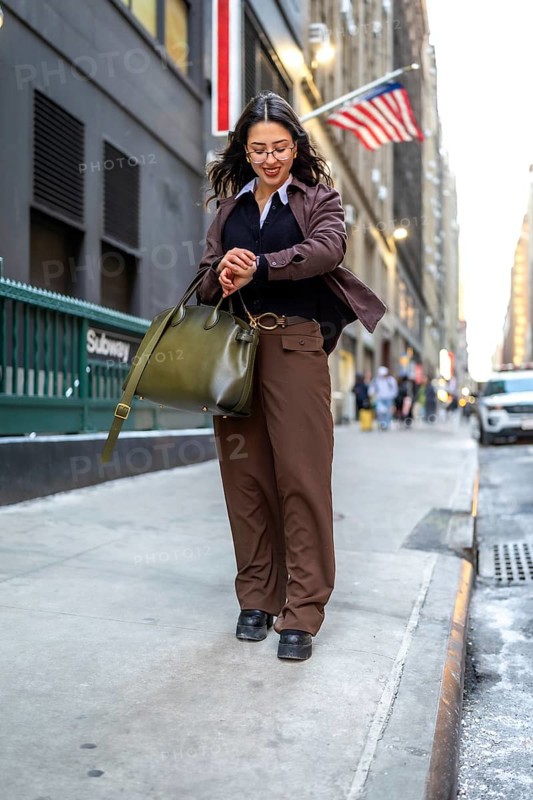 Young businesswoman walking urban street checking wrist watch while holding a handbag, representing punctuality, busy executive lifestyle, and urban commuting