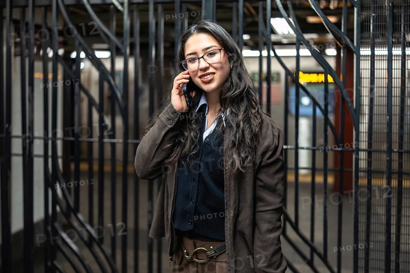 Young businesswoman standing in a new york city subway station, smiling while having a business phone call on her modern smartphone, reflecting urban professional life