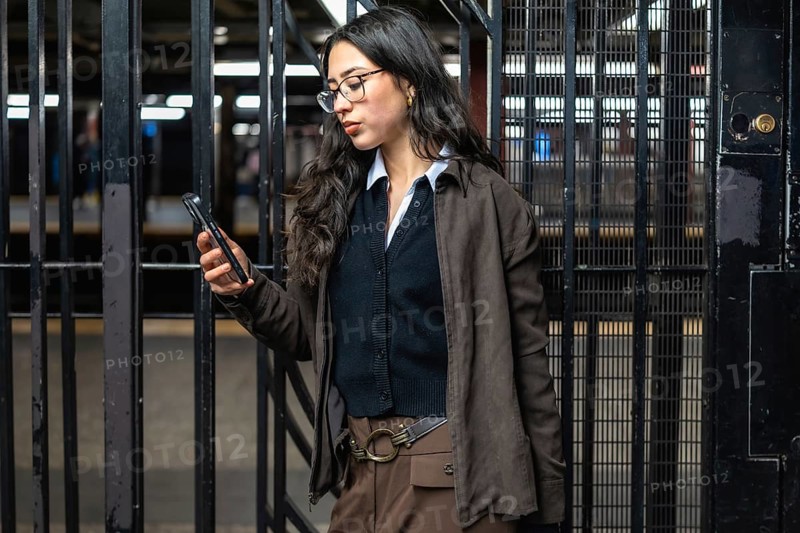 Young businesswoman standing in a new york city subway station, checking her mobile phone while commuting, representing modern urban connectivity and professional life