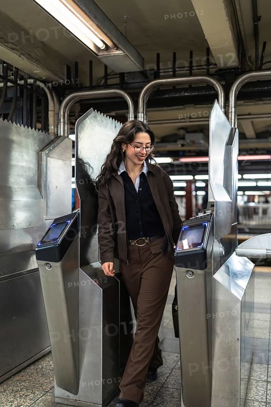 Young businesswoman with glasses and professional attire entering a new york city subway station turnstile, experiencing daily urban commute and public transportation
