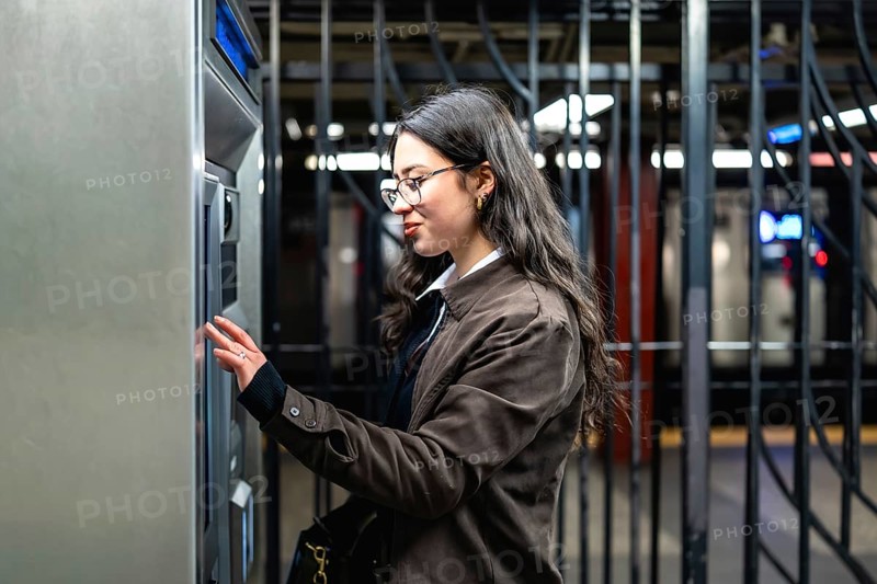 Young professional woman using a ticket machine in a new york city subway station, navigating urban commuting and public transport with a focused and determined expression
