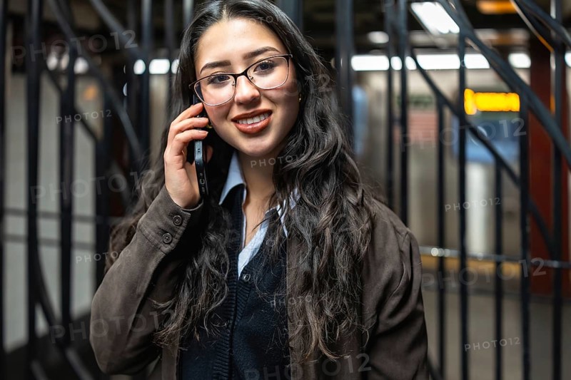 Young professional businesswoman smiling while making a phone call on her smartphone in a new york city subway station during her daily commute. Representing urban connectivity and corporate mobility