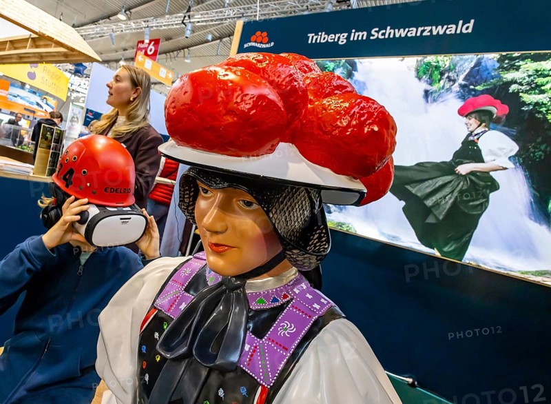 Tradition and progress. A young trade fair visitor wearing 3D glasses next to a model of a woman wearing traditional traditional costume and a Black Forest Bollenhut. Caravan — Motor — Tourism trade fair in Stuttgart. According to the exhibition organizer, CMT is the world's largest public trade fair for tourism and leisure. Stuttgart, Baden-Württemberg, Germany