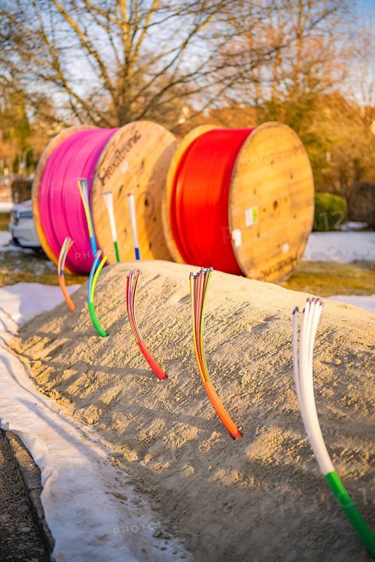 Colourful cables stick out of a snow hill, behind them colorful rolls of cable in winter light, fibreglass groundbreaking, Freudenstadt, Germany