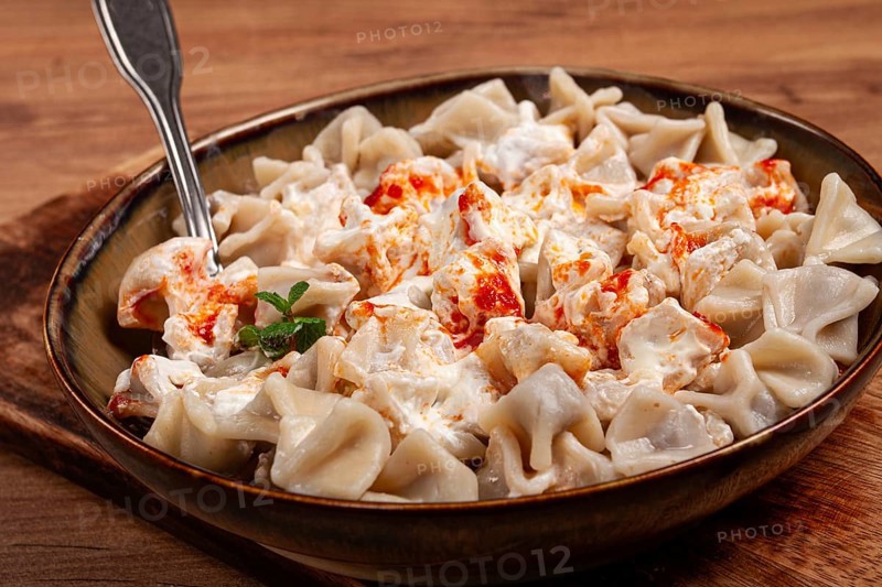 The dish features a generous serving of Turkish dumplings topped with velvety yogurt and a drizzle of spicy red sauce