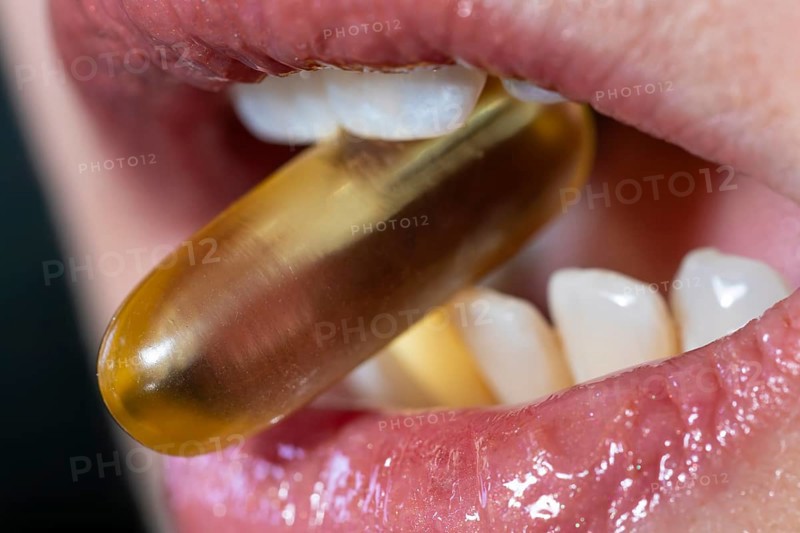 Close view of a woman mouth taking an omega 3 capsule