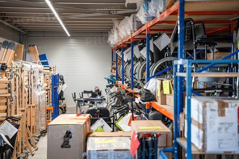 Storage room with shelves full of wheelchairs and boxes, industrial and organized, medical supply store