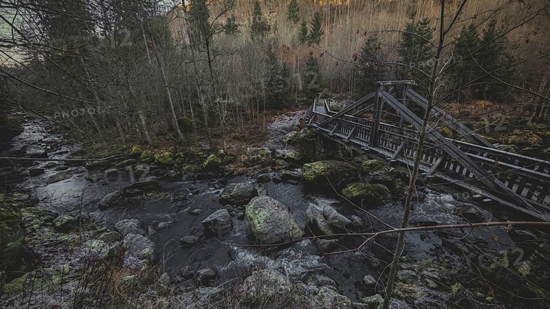 An old wooden bridge crosses a river in a dense, autumnal forest with a gloomy atmosphere, Teufelssteg im Höllental, Frankenwald nature park Park, Germany