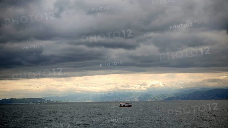 Small boat on calm sea under cloudy sky surrounded by mountains in the background, Lake Ohrid, North Macedonia