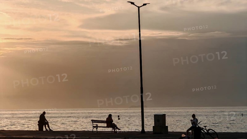 People sitting and bikers by the sea at sunset, quiet and peaceful atmosphere, waterfront, Izola, Slovenia