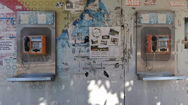 Two orange telephone boxes on a wall covered with graffiti and posters in an urban setting, Tirana, Albania
