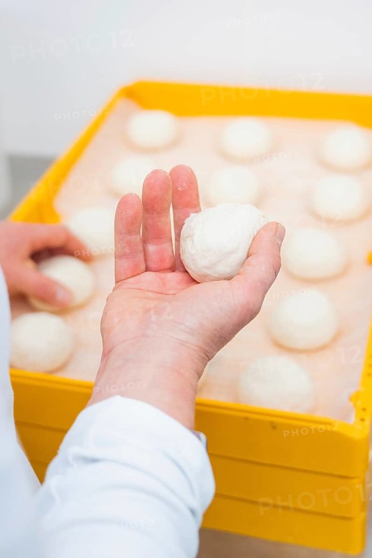 A baker holds a dough ball over several other dough balls in a yellow box, bake rolls, Haselstaller Hof, Gechingen, Germany