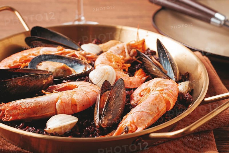 Seafood and black rice paella, in a frying pan, homemade, on a wooden table, no people