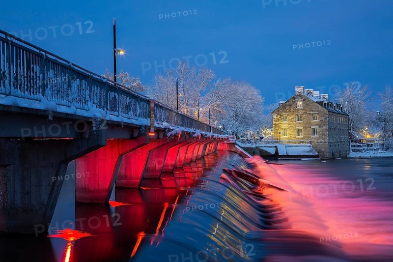 Illuminated Moulin Neuf water flow control dam and walkway over Des Mille-Iles river plus New Mill on Ile des Moulins with first winter like snow in late autumn at dusk, Old Terrebonne, Quebec, Canada