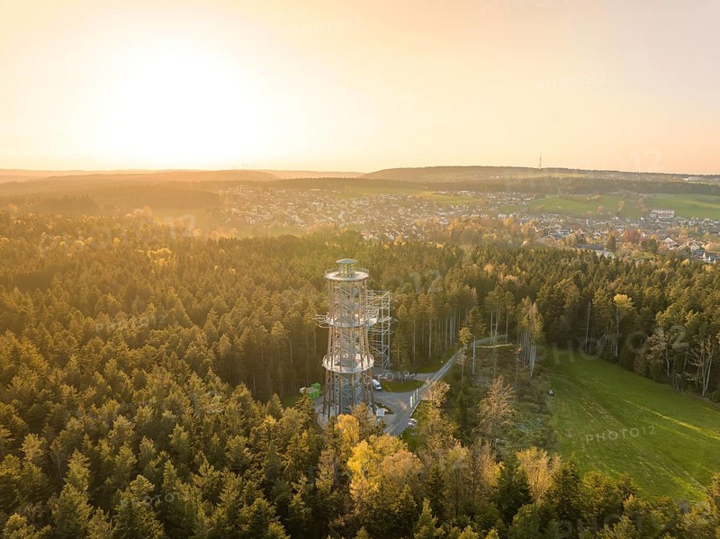 A tower towers over a forest, the view extends to a city in warm sunset light, Himmelsglück observation tower with Flying Fox, Schömberg, Black Forest, Germany