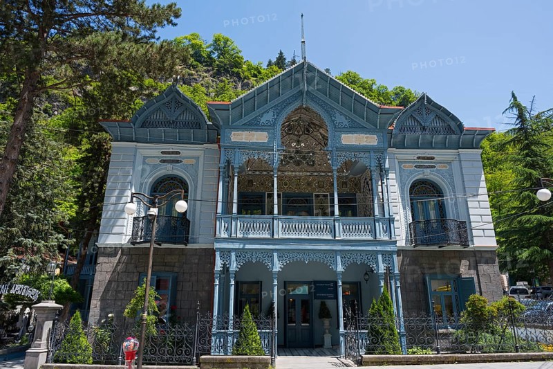 Magnificent historical architecture with an ornate blue veranda nestled in green nature, old villa of Mirza-Riza-Khan from the 19th century, cultural monument, Golden Tulip Borjomi resort, Borjomi, Kura river, Samtskhe—Javakheti region, Lesser Caucasus, Georgia