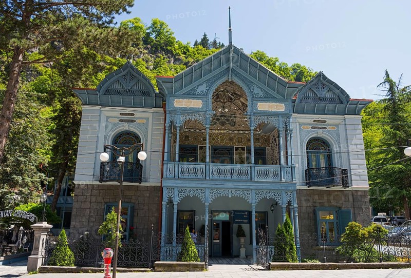 Historic blue building with abundant decorations and trees in the foreground, old villa villa of Mirza-Riza-Khan from the 19th century, cultural monument, Golden Tulip Borjomi resort, Borjomi, Kura river, Samtskhe—Javakheti region, Lesser Caucasus, Georgia