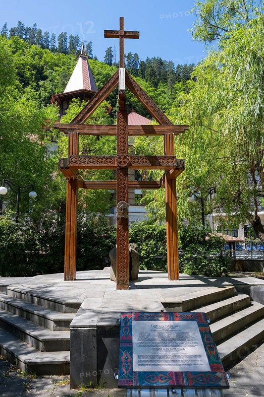 Wooden cross on a pedestal surrounded by green trees and a building, memorial to the tragedy of April 9, 1989 in Tbilisi, Borjomi resort, Borjomi, Kura river, Samtskhe—Javakheti region, Lesser Caucasus, Georgia