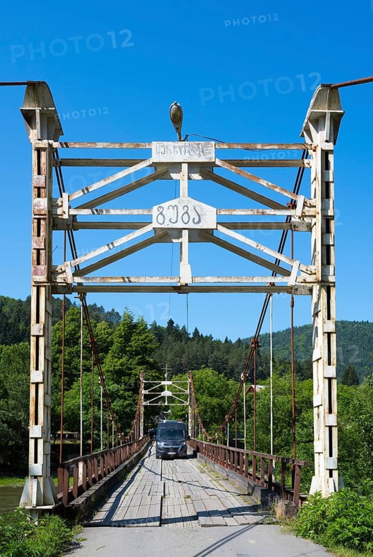 Car drives over an old suspension bridge surrounded by forest, camper, motorhome on a suspension bridge across the Kura River near Kortaneti, Samtskhe—Javakheti region, Georgia