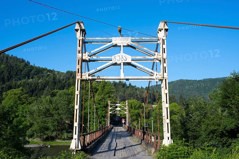 Steel bridge crosses a river amidst forested mountains, suspension bridge across the Kura River near Kortaneti, Samtskhe—Javakheti region, Georgia