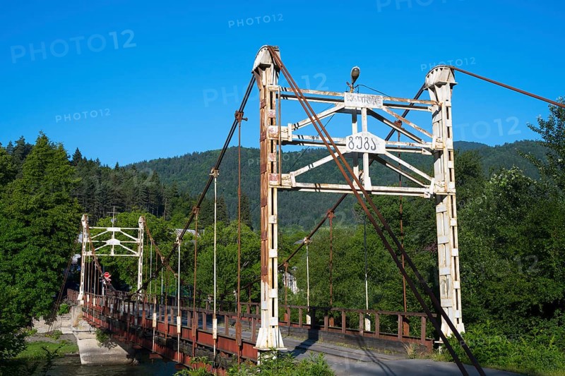 Old suspension bridge stretches across a river surrounded by green landscape, suspension bridge across the Kura River near Kortaneti, Samtskhe—Javakheti region, Georgia