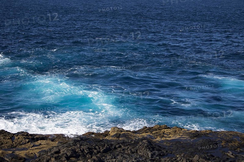 Waves break on a rocky coastline under deep blue skies, Yaiza Lanzarote