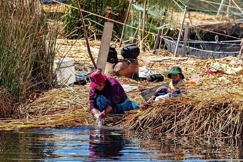 Woman and child work in a rural scene on the shores of a lake surrounded by reeds, The floating reed islands of the Uros in Lake Titicaca in Peru