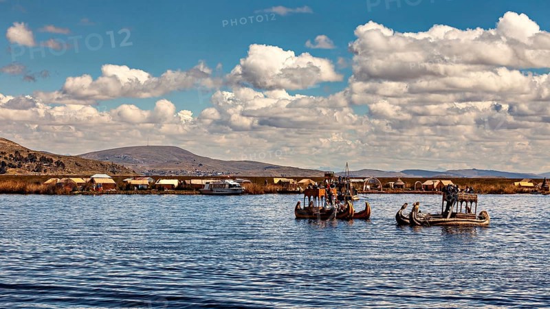 Traditional reed boats on a lake with a village on the shore under blue skies, The floating reed islands of the Uros in Lake Titicaca in Peru