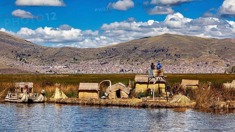Reed huts and lakeside observation tower in sunny weather with mountains in the background, The floating reed islands of the Uros in Lake Titicaca in Peru