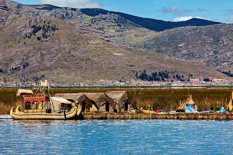 Reed boats and huts on a lake with mountains in the background, The floating reed islands of the Uros in Lake Titicaca in Peru