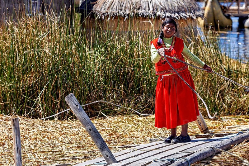 Woman in traditional dress rides a wooden reed boat in a lake, The floating reed islands of Uros in Lake Titicaca in Peru