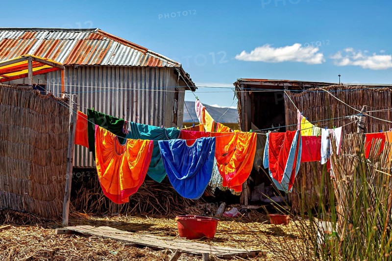 Colourful clothes hang on a line between traditional buildings under blue skies, The floating reed islands of the Uros in Lake Titicaca in Peru