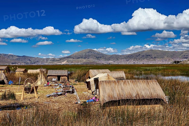A village with reed huts on a lake under a cloudy blue sky, The floating reed islands of the Uros in Lake Titicaca in Peru