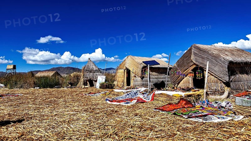 Traditional thatched huts on an island under a clear sky, The floating reed islands of the Uros in Lake Titicaca in Peru