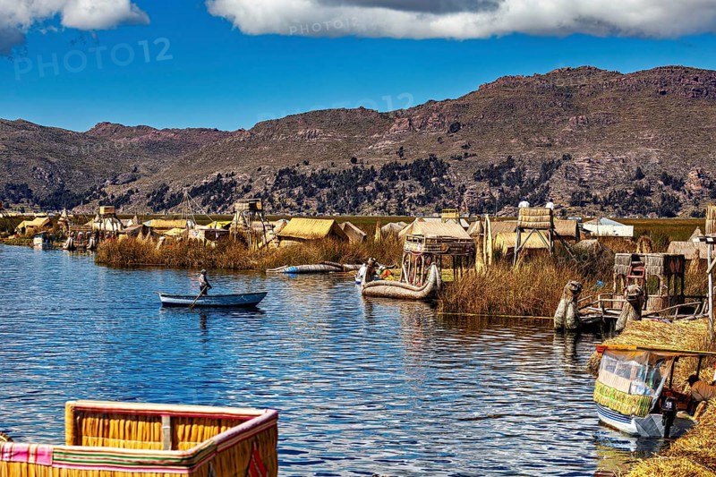 Canoe on a lake with traditionally built reed huts and mountains, The floating reed islands of the Uros in Lake Titicaca in Peru