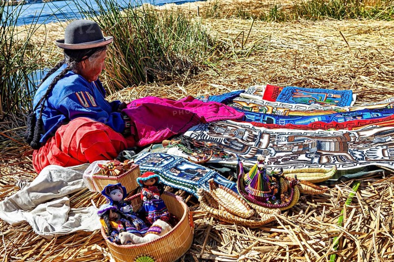 Woman sitting at colorful crafts on an island near a lake, The floating reed islands of Uros in Lake Titicaca in Peru