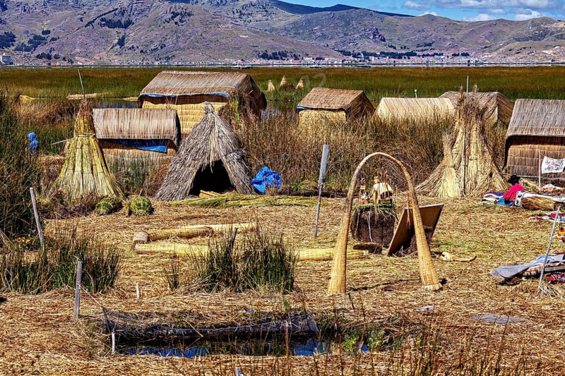 A peaceful village with reed huts and hills in the background, the floating reed islands of the Uros in Lake Titicaca in Peru