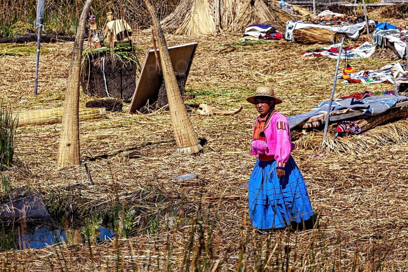 A woman in traditional dress stands in a quiet village made of reeds, The floating reed islands of the Uros in Lake Titicaca in Peru